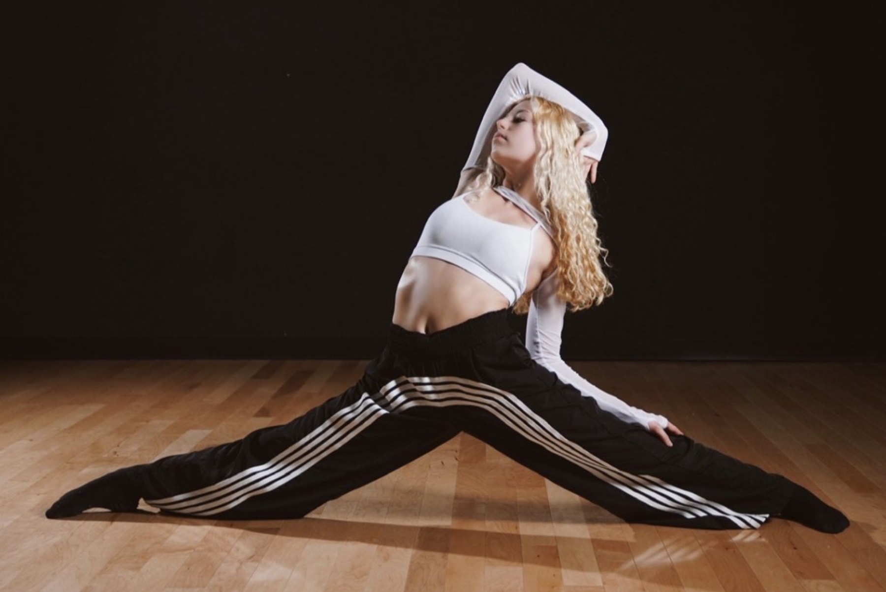 Gianna, a competitive dancer, holding a full center split on a studio floor with one arm curved overhead.